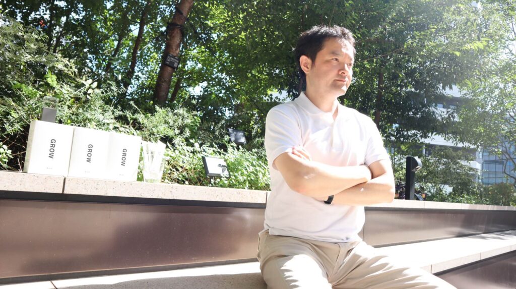 Fujikawa-san sits with his arms folded.
